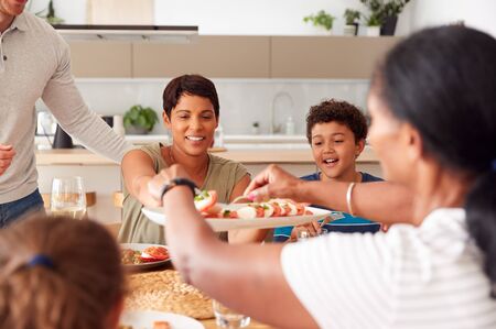 Father Serving As Multi-Generation Mixed Race Family Eat Meal Around Table At Home Togetherの写真素材