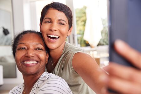 Mother With Adult Daughter Taking Selfie At Home Togetherの写真素材