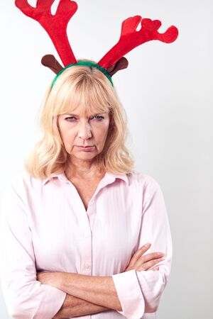 Studio Shot Of Unhappy Mature Woman Wearing Dressing Up Reindeer Antlers Against White Backgroundの写真素材