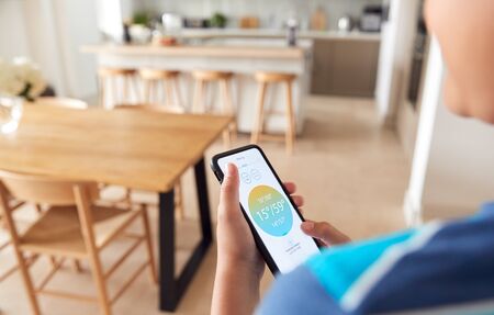 Close Up Of Boy Changing Temperature On Central Heating  Control Using Mobile Phone Appの写真素材