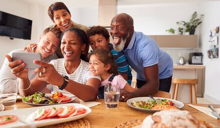 Multi-Generation Mixed Race Family Posing For Selfie As They Eat Meal Around Table At Home Together