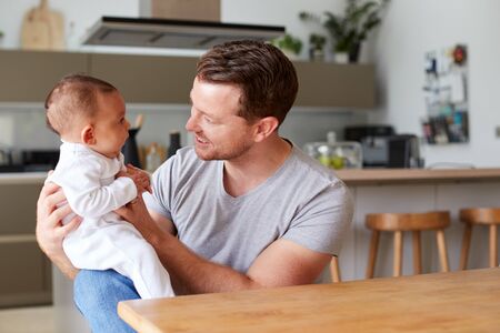 Loving Father Holding 3 Month Old Baby Daughter In Kitchen At Home