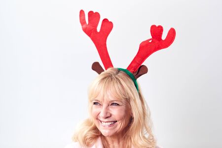 Studio Shot Of Happy Mature Woman Wearing Dressing Up Reindeer Antlers Against White Backgroundの写真素材