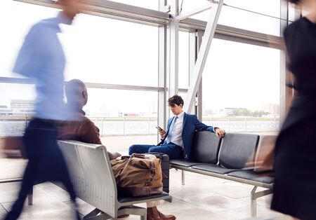 Business Passengers Sitting In Busy Airport Departure Lounge Using Mobile Phonesの写真素材