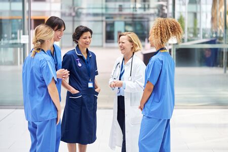 Female Medical Team Having Informal Meeting Standing In Lobby Of Modern Hospital Buildingの写真素材