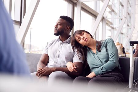 Tired Business Couple Sitting By Window Waiting In Airport Departure Lounge