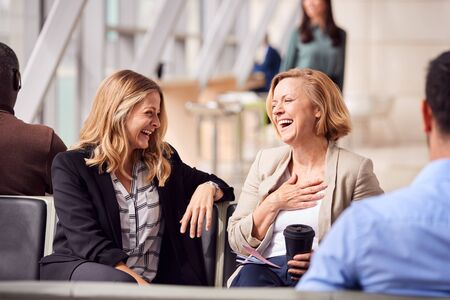 Two Businesswomen Sitting In Airport Departure Talking Togetherの写真素材
