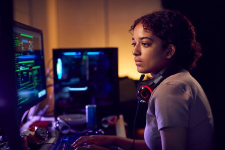 Female Teenage Hacker Sitting In Front Of Computer Screens Bypassing Cyber Securityの写真素材