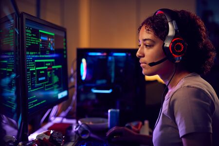 Female Teenage Hacker Sitting In Front Of Computer Screens Bypassing Cyber Securityの写真素材