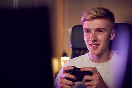 Teenage Boy With Game Pad Sitting In Chair and Gaming At Homeの写真素材