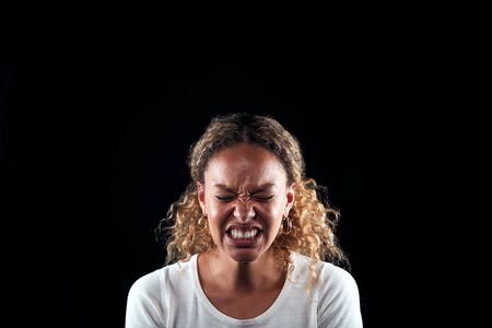 Studio Portrait Of Angry Woman Shouting At Camera Against Black Background