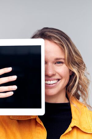 Studio Portrait Of Smiling Young Woman Covering Face With Digital Tabletの写真素材