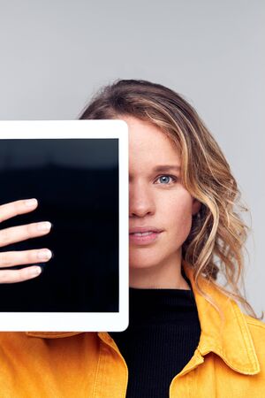 Studio Portrait Of Smiling Young Woman Covering Face With Digital Tabletの写真素材