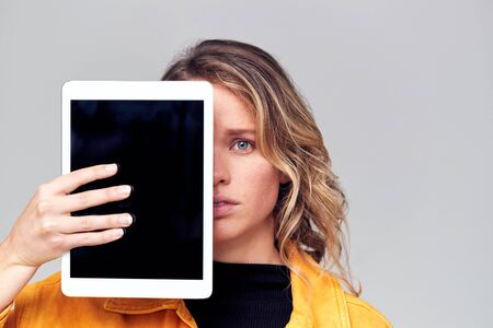 Studio Portrait Of Worried Young Woman Covering Face With Digital Tabletの写真素材