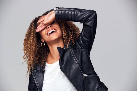 Studio Shot Of Happy Young Woman Wearing Leather Jacket Covering Face With Handの写真素材