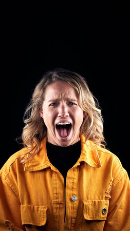 Studio Portrait Of Angry Woman Shouting At Camera Against Black Background