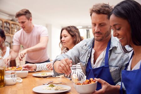 Group Of Men And Women Sitting Around Table Eating Meal They Have Prepared In Kitchen Cookery Classの写真素材