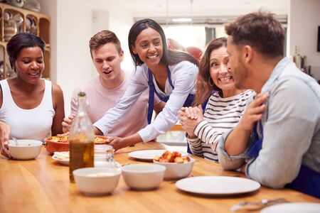 Group Of Friends Sitting Around Table Eating Meal At Home Togetherの写真素材