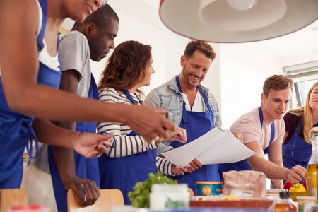 Male And Female Adult Students Looking At Recipe In Cookery Class In Kitchenの写真素材