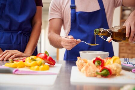Male And Female Adult Students Adding Olive Oil To  Dish In Kitchen Cookery Classの写真素材