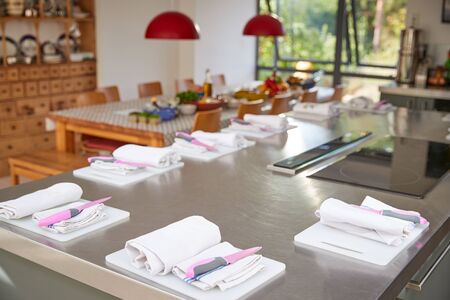 Aprons And Knives Laid Out On Chopping Boards In Kitchen Set For Cookery School