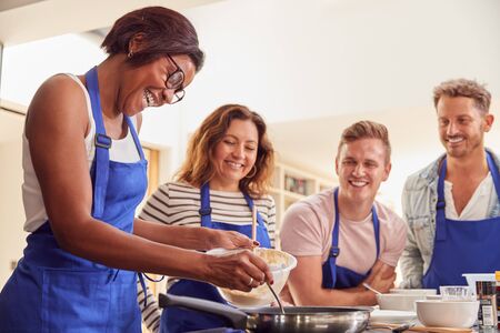Female Teacher Making Pancake On Cooker In Cookery Class As Adult Students Look Onの写真素材