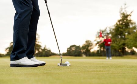 Close Up Of Female Golfer Putting Ball On Green As Man Tends Flagの写真素材