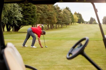 Mature Male Golfer Preparing To Hit Tee Shot Along Fairway With Driver Viewed Through Buggy Windowの写真素材
