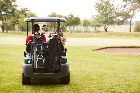 Rear View Of Couple Playing Golf Driving Buggy Along Fairway On Red Letter Dayの写真素材