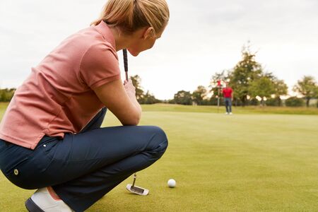 Female Golfer Lining Up Shot On Putting Green As Man Tends Flagの写真素材
