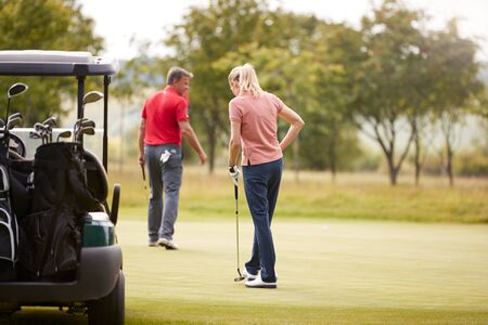 Rear View Of Couple Getting Out Of Golf Buggy To Play Shot On Greenの写真素材