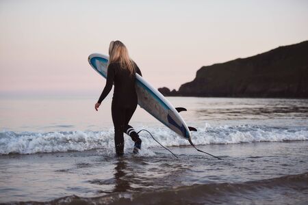 Woman Wearing Wetsuit Carrying Surfboard As She Walks Into Seaの写真素材
