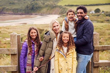 Portrait Of Active Multi-Cultural Family Standing By Gate On Winter Beach Vacationの写真素材