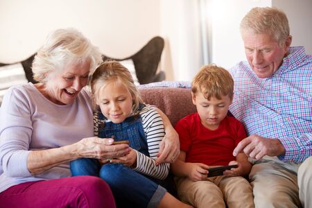 Grandparents Playing Video Games With Grandchildren On Mobile Phones At Homeの写真素材