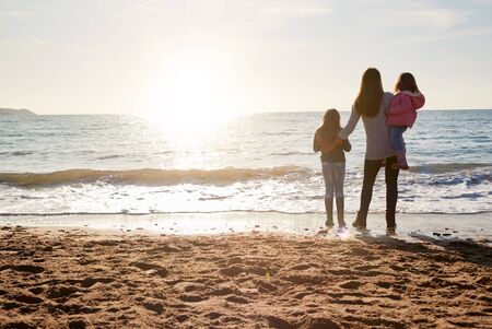 Rear View Of Mother With Daughters Looking Out To Sea Silhouetted Against Sunの写真素材