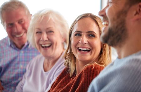 Senior Parents With Adult Offspring Sitting On Sofa At Home Talking And Laughingの写真素材