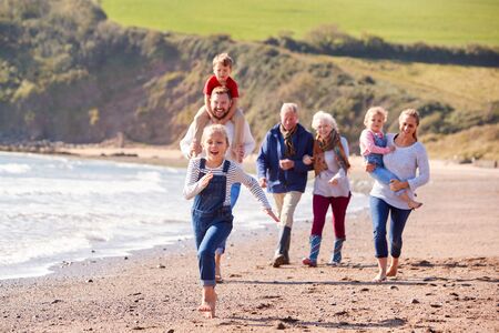 Multi-Generation Family Walking Along Shoreline Of Beach By Waves Togetherの写真素材