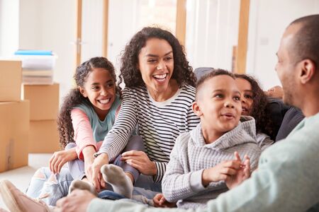 Family Taking A Break And Sitting On Sofa Celebrating Moving Into New Home Togetherの写真素材