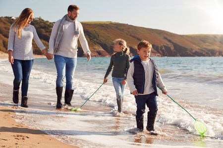 Family With Fishing Nets Walking Along Shoreline Of Winter Beachの写真素材
