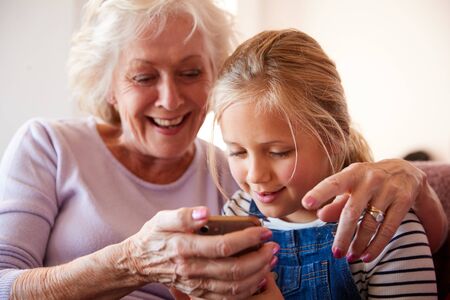 Grandmother Playing Video Game With Granddaughter On Mobile Phone At Homeの写真素材