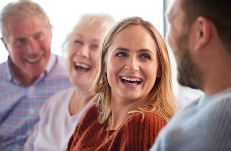 Senior Parents With Adult Offspring Sitting On Sofa At Home Talking And Laughing