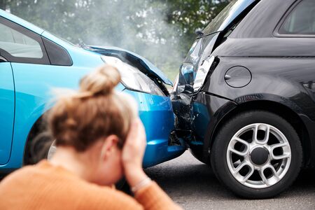 Female Motorist With Head In Hands Sitting Next To Vehicles Involved In Car Accidentの写真素材