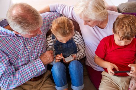 Grandparents Playing Video Games With Grandchildren On Mobile Phones At Home