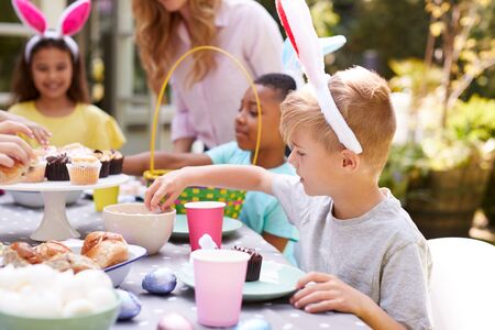 Mother With Children Wearing Bunny Ears Enjoying Outdoor Easter Party In Garden At Homeの写真素材