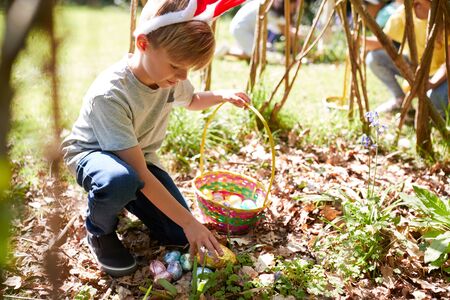 Group Of Children Wearing Bunny Ears Finding Easter Eggs Hidden In Garden