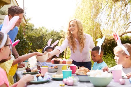 Parents With Children Wearing Bunny Ears Enjoying Outdoor Easter Party In Garden At Home