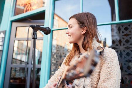 Female Musician Busking Playing Acoustic Guitar And Singing Outdoors In Streetの写真素材