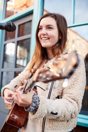 Female Musician Busking Playing Acoustic Guitar And Singing Outdoors In Streetの写真素材