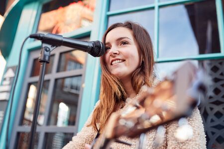 Female Musician Busking Playing Acoustic Guitar And Singing Outdoors In Streetの写真素材