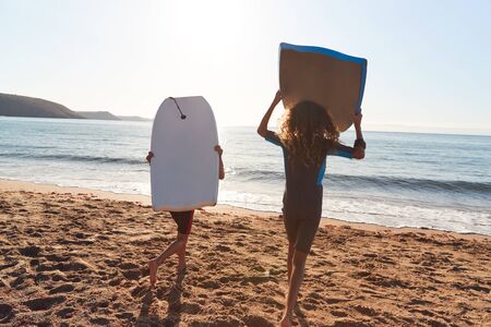 Children Wearing Wetsuits Carrying Bodyboards On Summer Beach Vacation Having Fun By Sea